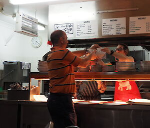 Expeditioner reaching over counter to collect parcel of fish and chips
