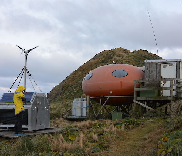 Louise standing in front of the power generator at Brothers Point hut