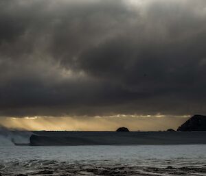 Clean breaking surf in front of a cloudy sky with low sunlight shining through