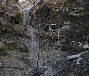 Two ladders and a toolbox in a rocky, icy gully.
