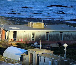 Wooden building with sun shining on its walls and ocean in background