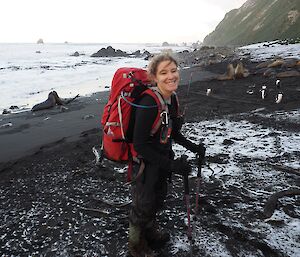 Anna standing on beach wearing red backpack with elephant seals in background