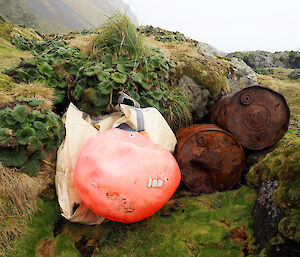 two drums and a big red marine buoy beside a rock ledge