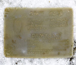 A waxy looking drift card, worn by ocean water, reads “drift card, Cape Town, South Africa”