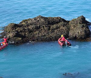 Two red boats slowly driving towards a rock