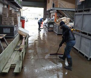 Person with broom sweeping water out of large doors