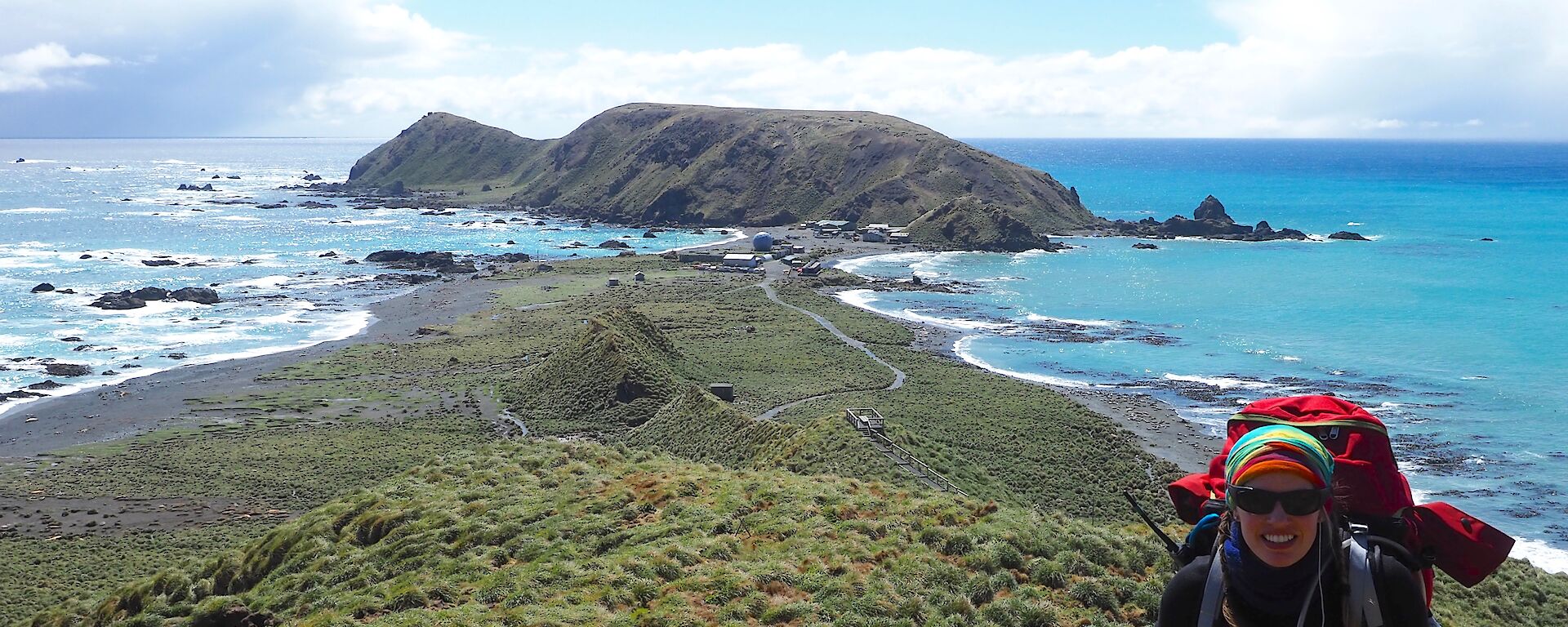 Female expeditioner climbing Doctors track with North Head in background — water flanks either side of the isthmus and station behind