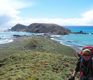 Female expeditioner climbing Doctors track with North Head in background — water flanks either side of the isthmus and station behind