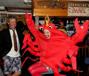 An expeditioner in suit jacket and tie but Hawaiian style shorts looks at a female expeditioner dressed as a giant crab