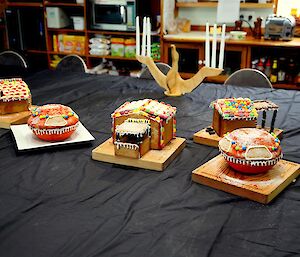 Five colourfully decorated gingerbread houses constructed to represent the huts on Macquarie Island. In the background is a handmade wooden albatross candelabra with six long white candles.