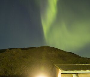 A thick green curtain of aurora australis blazes across the sky above Wireless HIll, just north of the station. In the foreground one of the accommodation buildings is well lit due to the long exposure time.