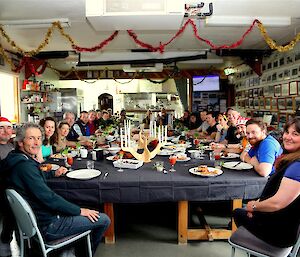 Expeditioners sitting down to a large table set with lots of food for brunch on Christmas Day. Tinsel decorations hang from the ceiling.