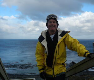Malcolm standing in a yellow jacket on stairs with ocean in background