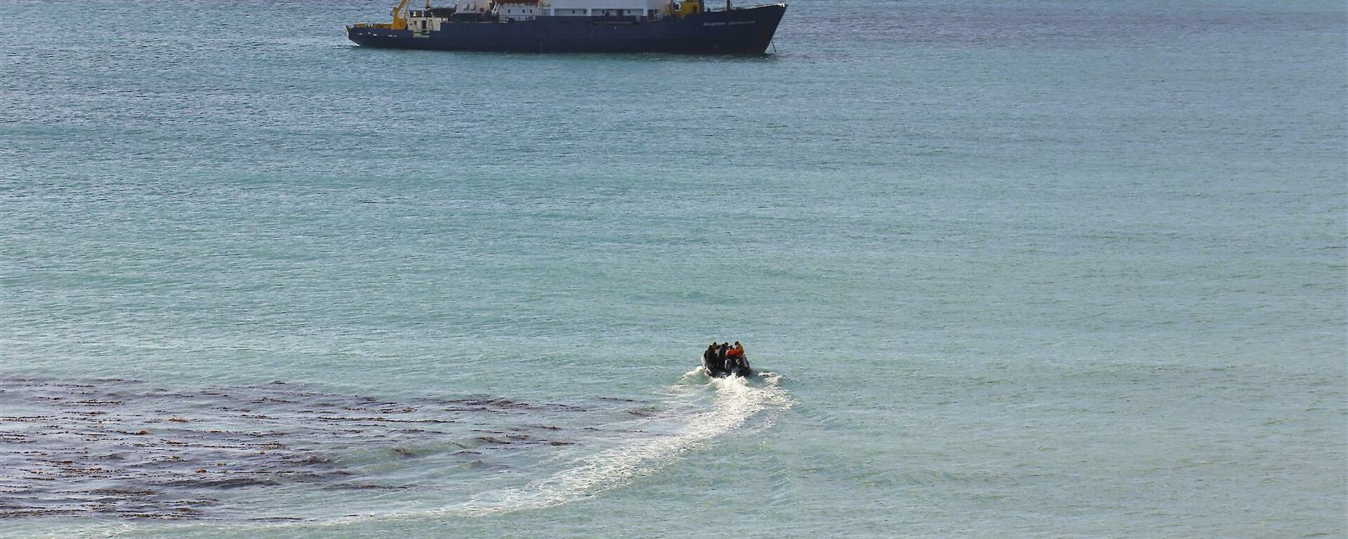 Small inflatable boat driving towards ship
