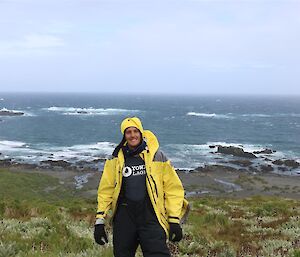 Tim A in yellow jacket with ocean and rocks behind