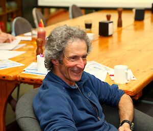 Male expeditioner sitting at a table, smiling at something off camera