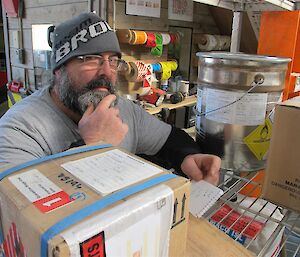 Close up of an older, bearded male expeditioner holding his chin in thought while organising parcels for return to Australia