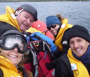 Four expeditioners smile from an inflatable rubber boat