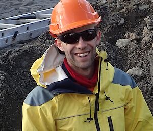 A male expeditioner stands in a hole wearing safety gear including a hard hat