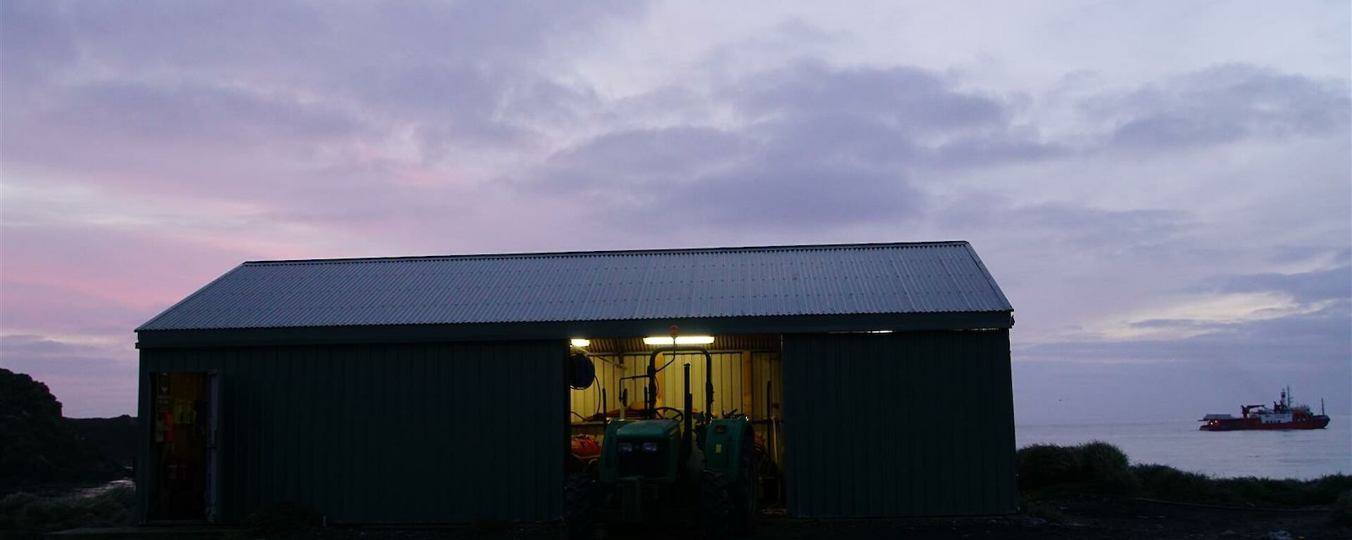 A pink sunrise sky over the boat shed with L'Astrolabe in the background
