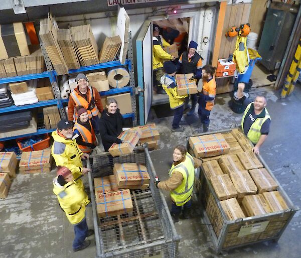 Shot from above of expeditioners unloading palleted frozen food and passing it along the line into the freezer