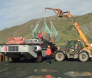 A net of old fuel drums being loaded by JCB onto a LARC for return transport to Australia for disposal