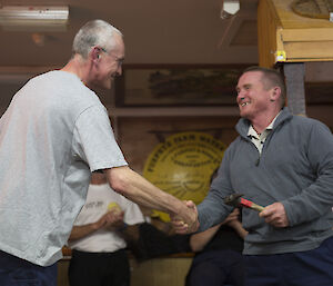 Two men shake hands and grin