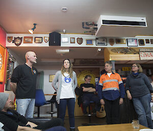 Two men and two women stand in front of a group in a lounge and bar area