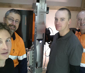 Four men stand inside. In the middle of them there is a metal beam and some other scientific and electrical instruments making up part of a LIDAR