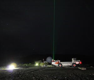 A thin laser beam pierces the night sky. We can see the geometric ANARESAT dome and a metal LARC (land and water) vehicle.