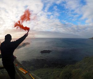 Ranger Chris farewells the ship with an orange smoke flare. Ocean and distant ship in background.