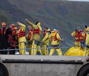 Deck of a LARC land/water vehicle with expeditioners in their yellow survival clothes waving goodbye