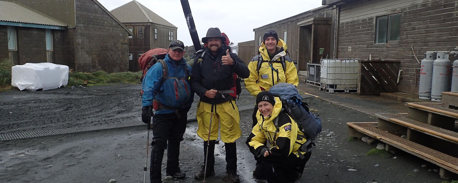 Four people stand in the main square of station kitted out in wet weather clothing and with field packs ready to leave on their familiarisation trip