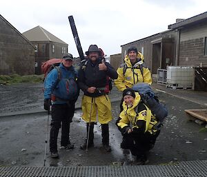 Four people stand in the main square of station kitted out in wet weather clothing and with field packs ready to leave on their familiarisation trip