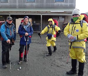 Four people kitted out in waterproofs and with packs and walking sticks smile for the camera in Market Square