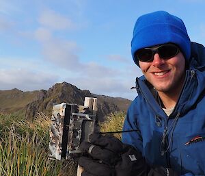 Man smiles at camera while holding a trail camera