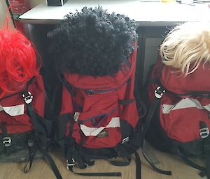 Three field packs in a row with different coloured wigs sitting on top of them to represent the missing people