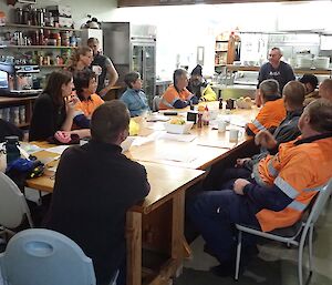 People sitting around a large dining table in the mess/dining room for a debrief on the exercise — the table is littered with paper, notepads, ipads and more