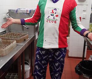 A man stands in the kitchen wearing his football team’s short and trousers.