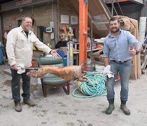 Two men carry a cooked lamb still on its spit