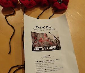 Knitted poppies and a printed ANZAC day service program with ‘Lest we forget’ on the cover
