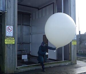 A woman exits a tall shed holding a large balloon