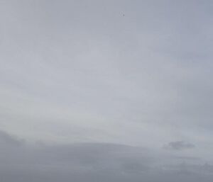 A shot of the ocean and sky with a balloon travelling in the sky