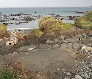 A piece of land next to the coast with dirt, an old pipe and some upright markers.