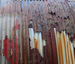 A close up of the corrugated iron sheeting showing the various colours of previous painted layers and the level of rust