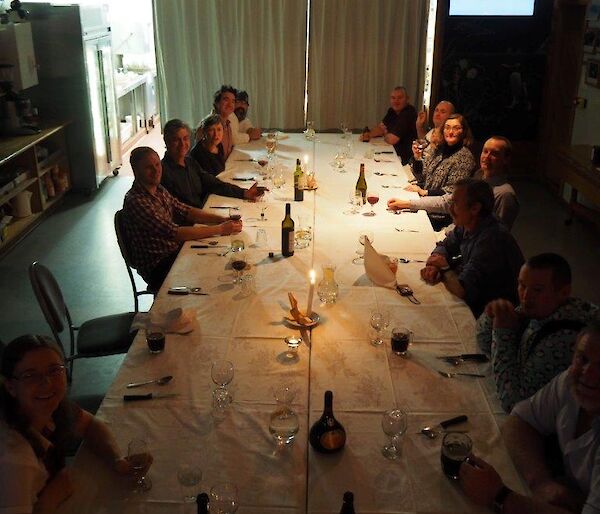 A group of people sitting around a large table set with white lines and candles.