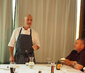 A man in chef’s clothes stands in front of the table