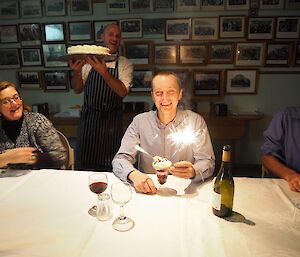 A man smiles at camera as a birthday cake is presented to him