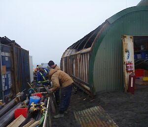3 men working in front of the half stripped shed