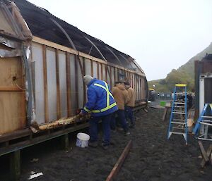 3 men work at the side of the building pulling out old insulation.